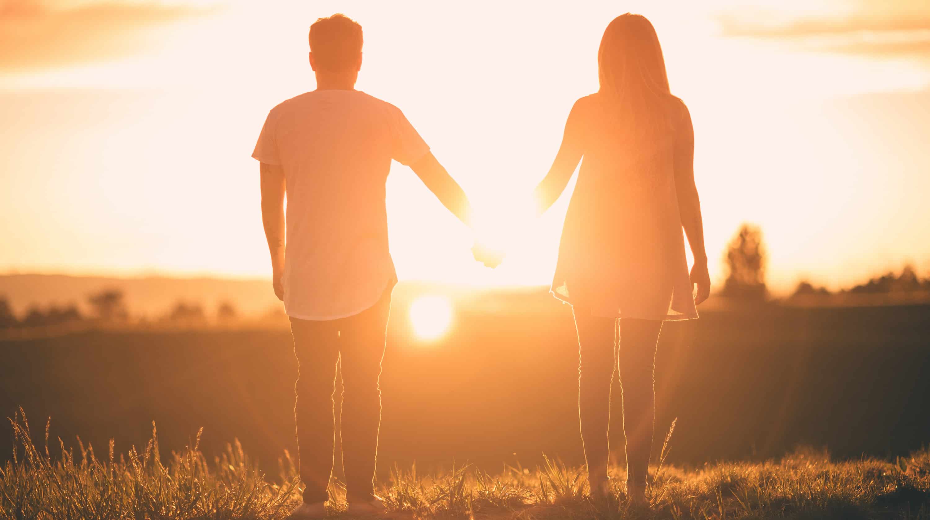 A man and woman hold hands while looking at a sunset.