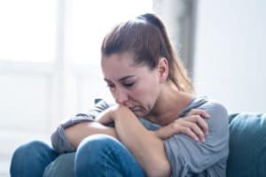 Depressed woman sitting on couch, hugging a couch cushion for comfort