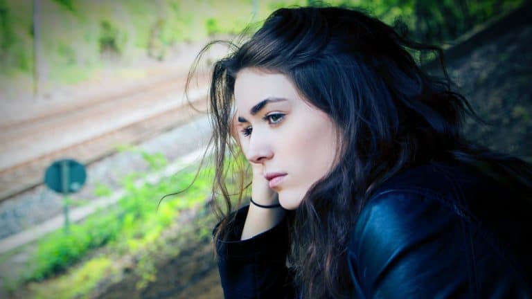Serious-looking dark-haired woman leaning her head on her hand, looking into the distance