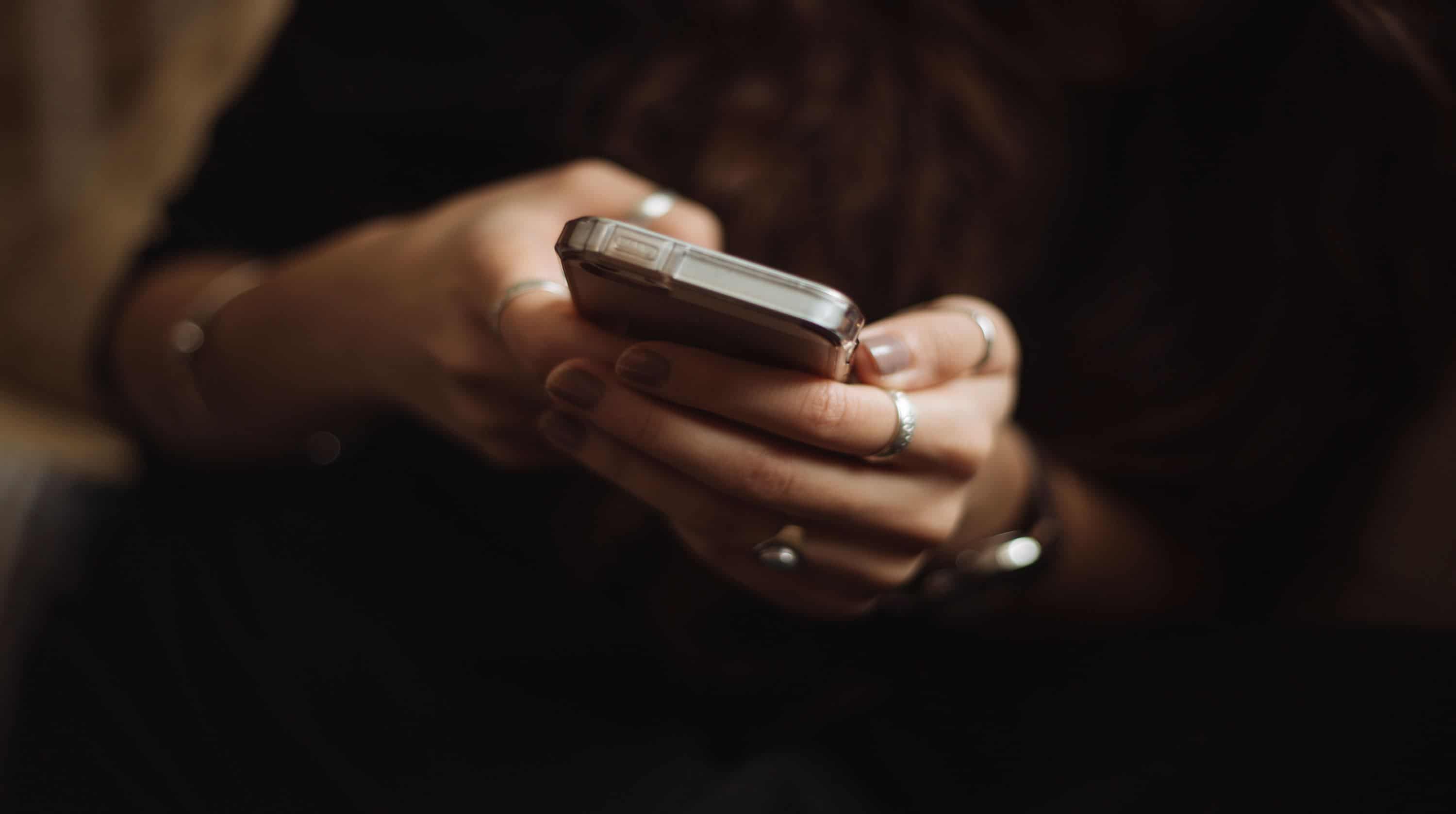 Woman holding a phone with rings on her fingers.