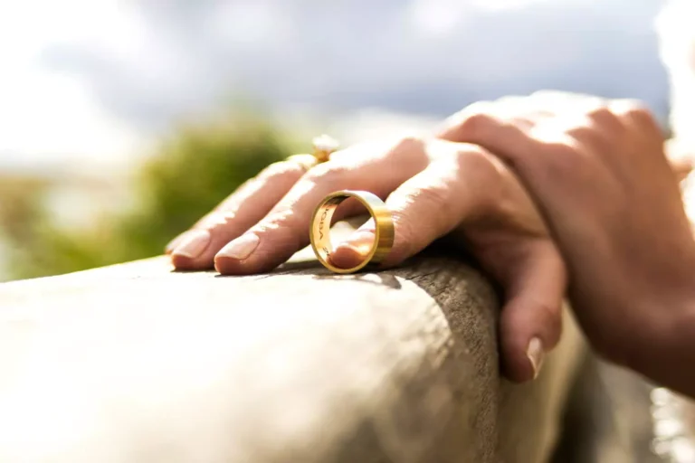 A close-up of a hand loosely holding a gold wedding ring, symbolizing the difficult decision of knowing when it is appropriate to leave a marriage.