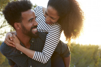 Laughing, young, black couple having fun as he gives her a piggyback ride outside