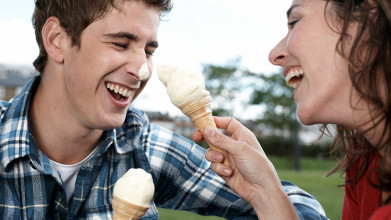 Close up of laughing young couple holding ice cream cones. She has just playfully touched his nose with hers.