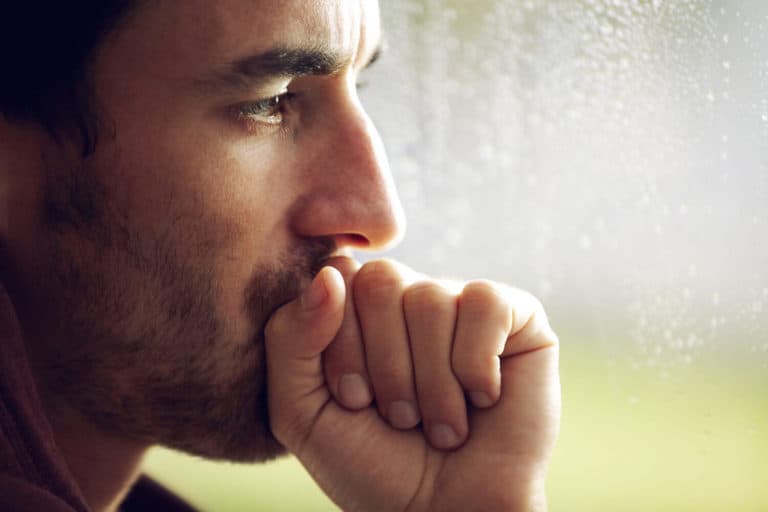 Close up profile of a man's face, with his balled-up hand resting against his mouth like he’s deep in thought.