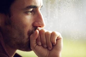 Close up profile of a man's face, with his balled-up hand resting against his mouth like he’s deep in thought.