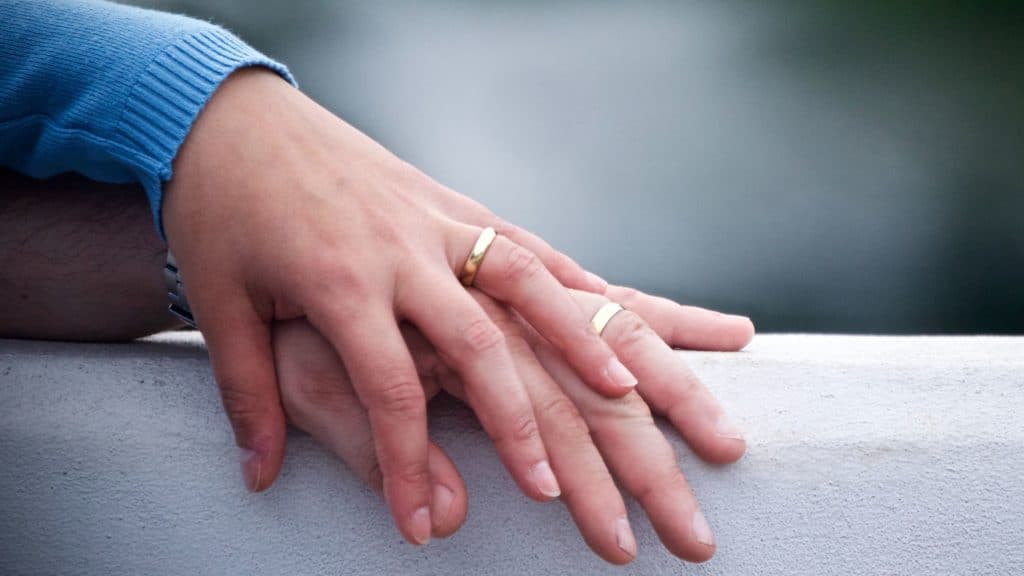 woman's hand resting on man's hand with wedding bands
