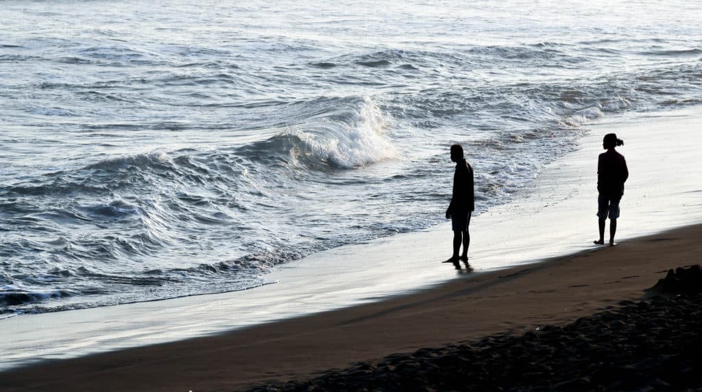 A couple walks apart from each other at sunset on the beach.