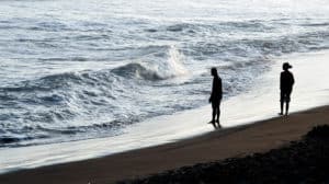 A couple walks apart from each other at sunset on the beach.