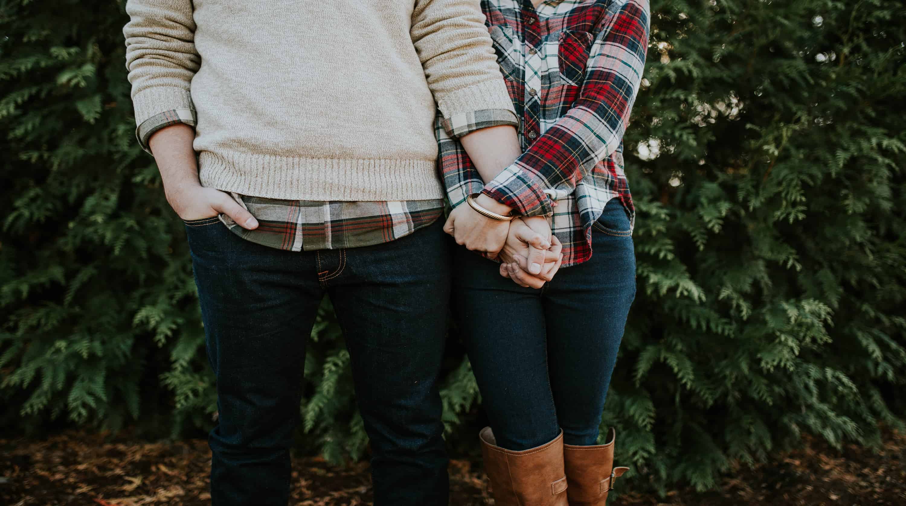 A couple is holding hands and wearing flannel shirts on a fall day.