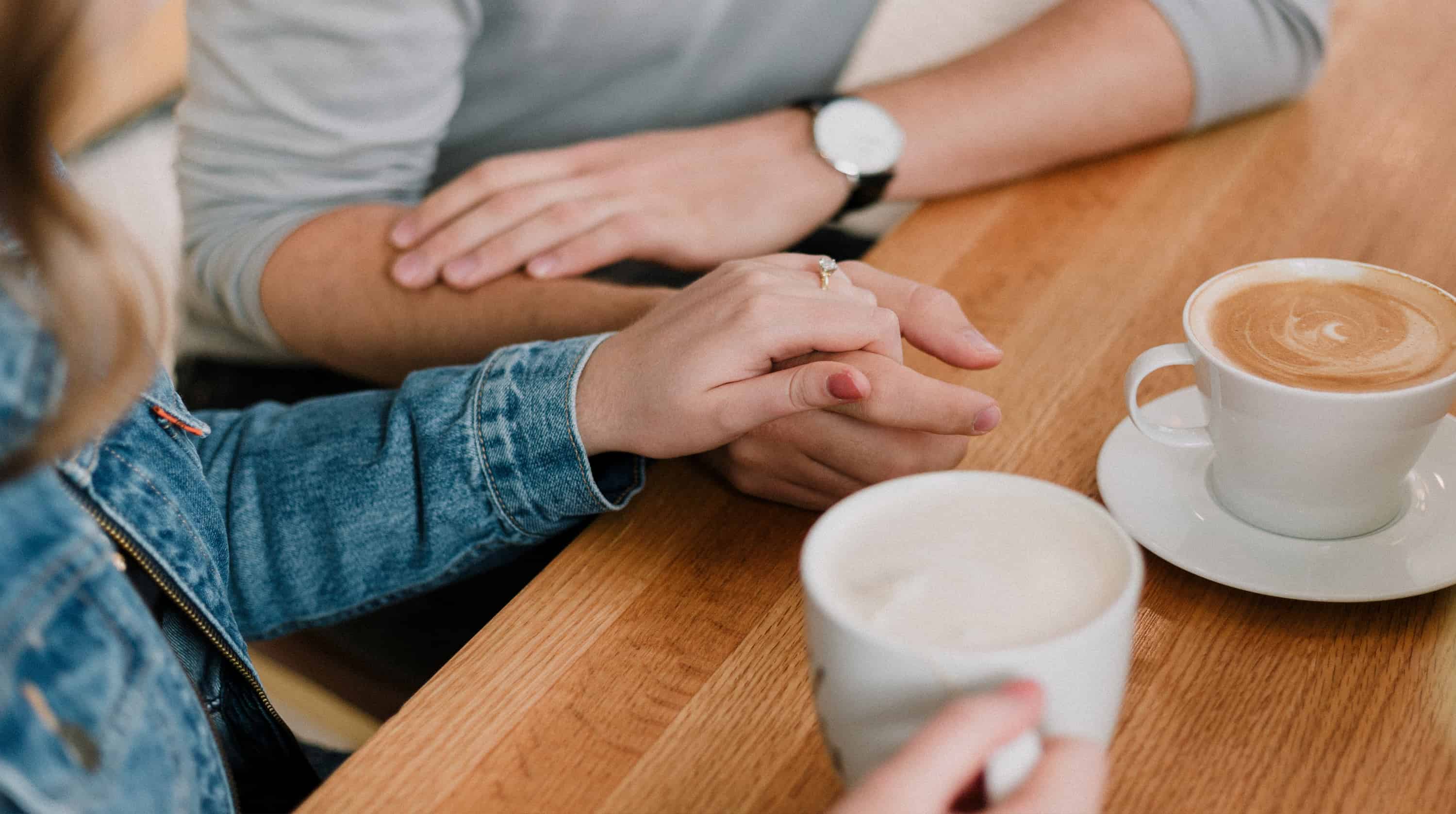 Awomanis hold ing a man's hand while drinking coffee.