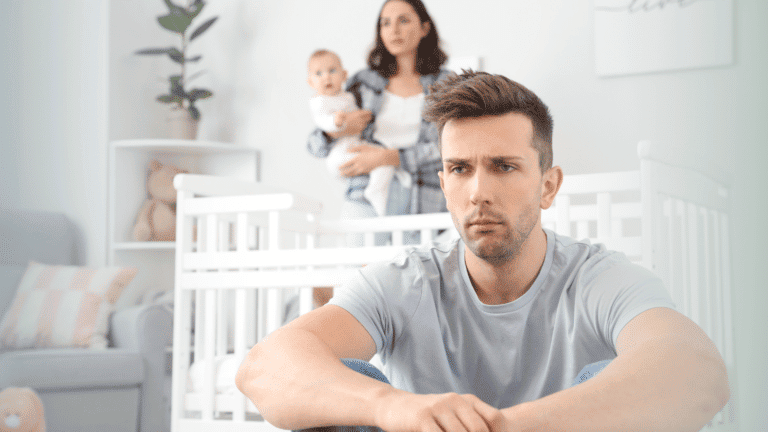 Depression in a Christian Family is real. This image is a depressed man sitting staring off into space with his wife and baby in the background