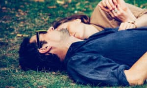 A married couple lay side by side in the grass on a fall day.