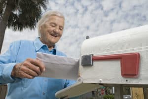 Smiling grandfather standing at his mailbox retrieving a letter he received