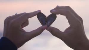 two hands holding black rocks in shape of heart