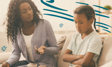 Mother sitting on couch with daughter and disciplining her.