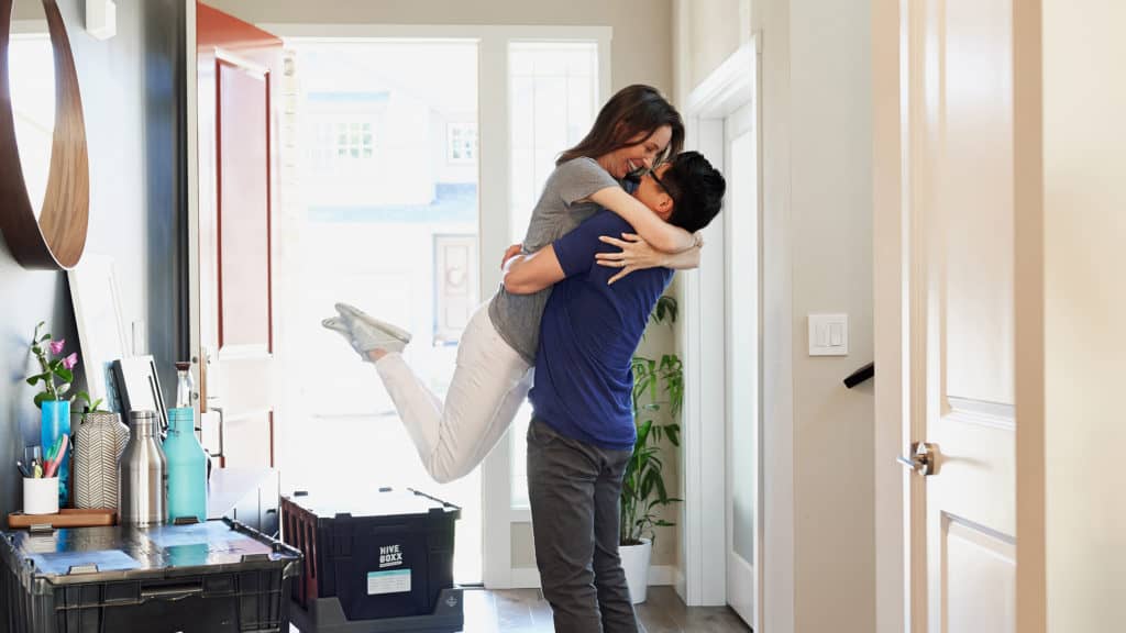 a woman jumps into a man's arms as they unpack moving boxes.