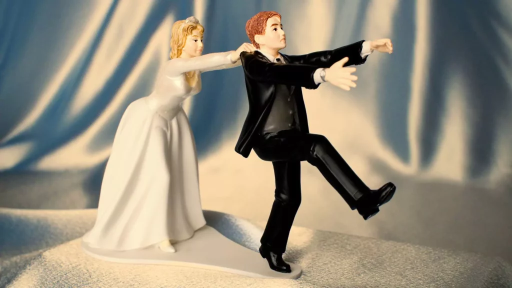 A cake-topper depicting a groom attempting to flee because he's having second thoughts about the wedding, but the bride holds him back.