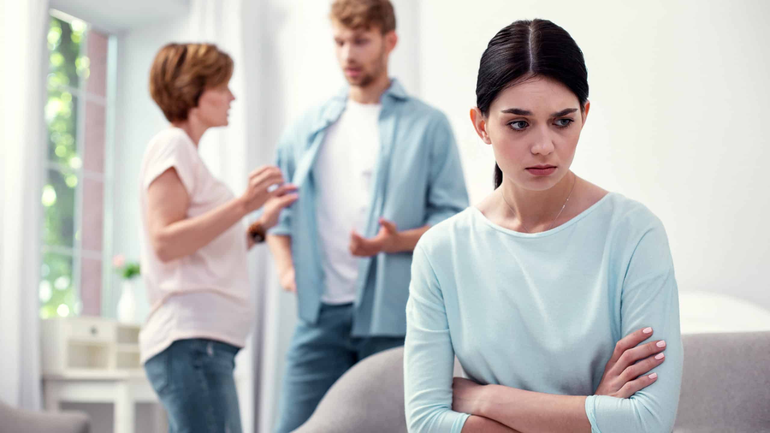 young woman upset listening to husband and mother in law in background