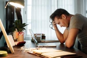 Young man sitting in front of his laptop, leaning his head against his hand and looking stressed-out