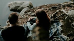 man and woman sitting on blanket at edge of water