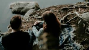 man and woman sitting on blanket at edge of water