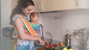 Homemaking Mother with her baby in a carrier making dinner