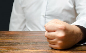 Close up of a man's fist resting on a table, suggesting it's balled up in anger