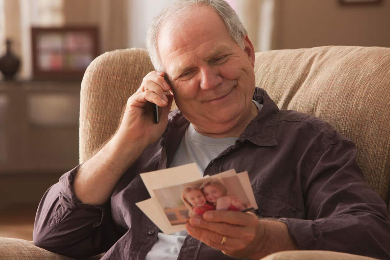 Older man sits in comfortable chair enjoying photos of grandchildren