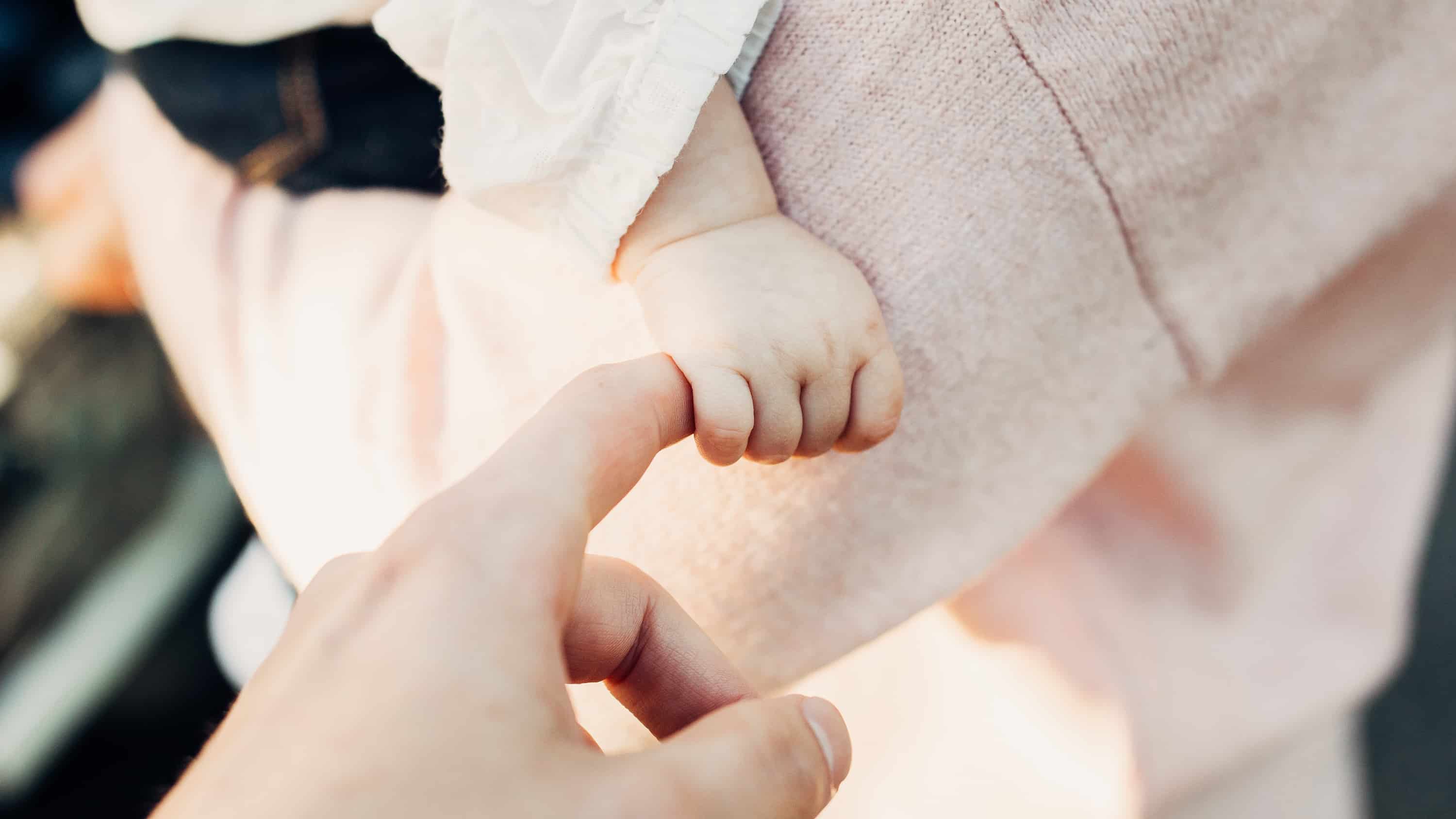 A man's fingers is grasped by the tiny hand of a baby.