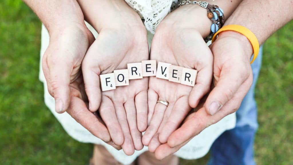 Two hands holding scrabble letters that spell forever