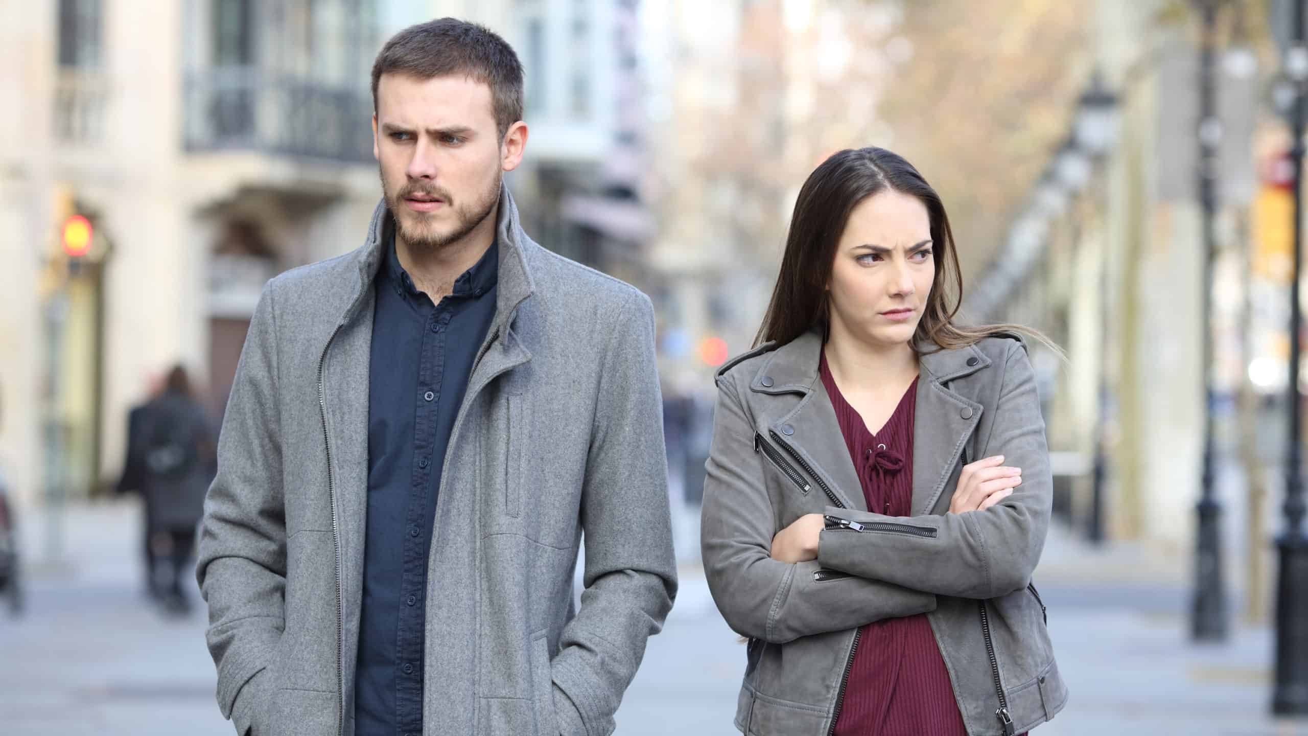 man and woman in jackets standing on sidewalk angry