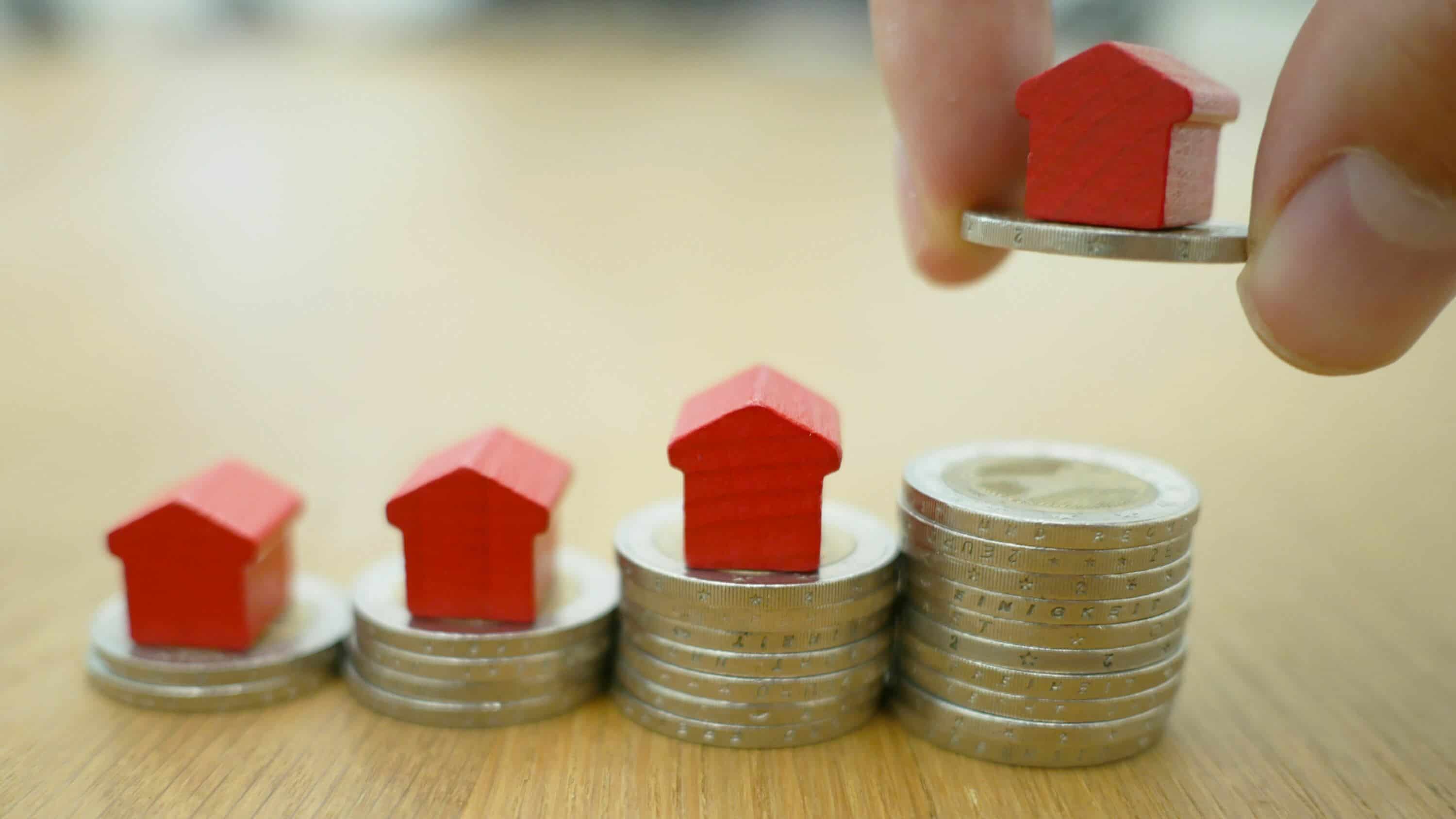 Person placing quarter in stacks with little red wood house figurine on top