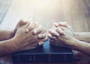 Close up of a couple's folded hands resting on a Bible