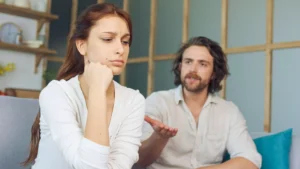 A young couple sit on a couch in conflict. Healthy conflict in marriage is key to loving your spouse.