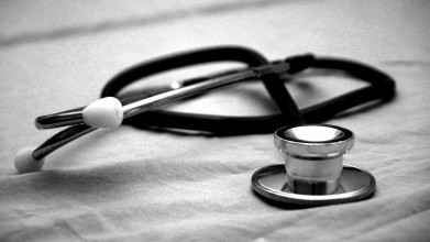 Black and white close up of a stethoscope lying curled up on a bedsheet