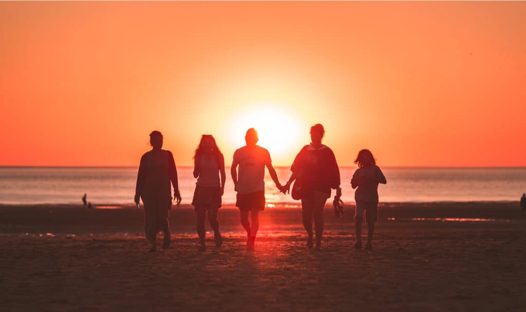 A family walks together together down the beach holding hands.
