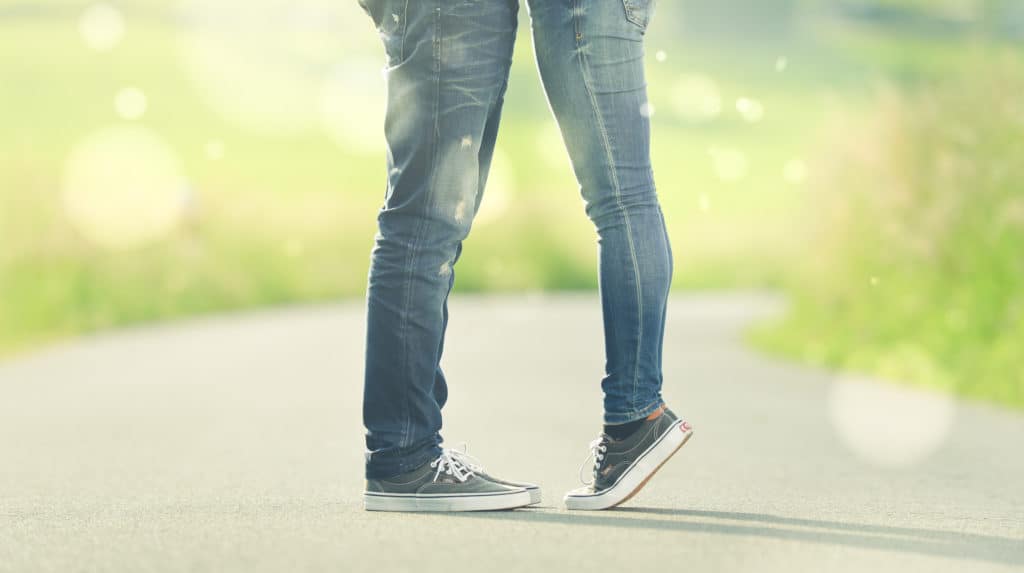 A woman and a man wearing jeans stand facing each other.