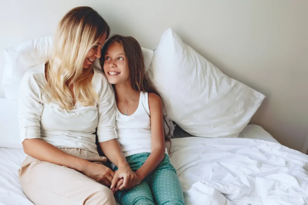 mom and tween daughter sitting on a bed talking