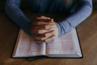 folded hands praying over the bible