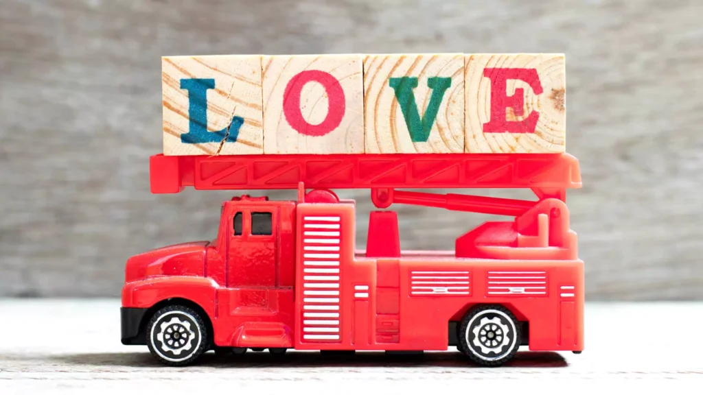 A small red toy fire truck holds wooden blocks spelling out “LOVE,” symbolizing the strength and importance of love in a first responder marriage.