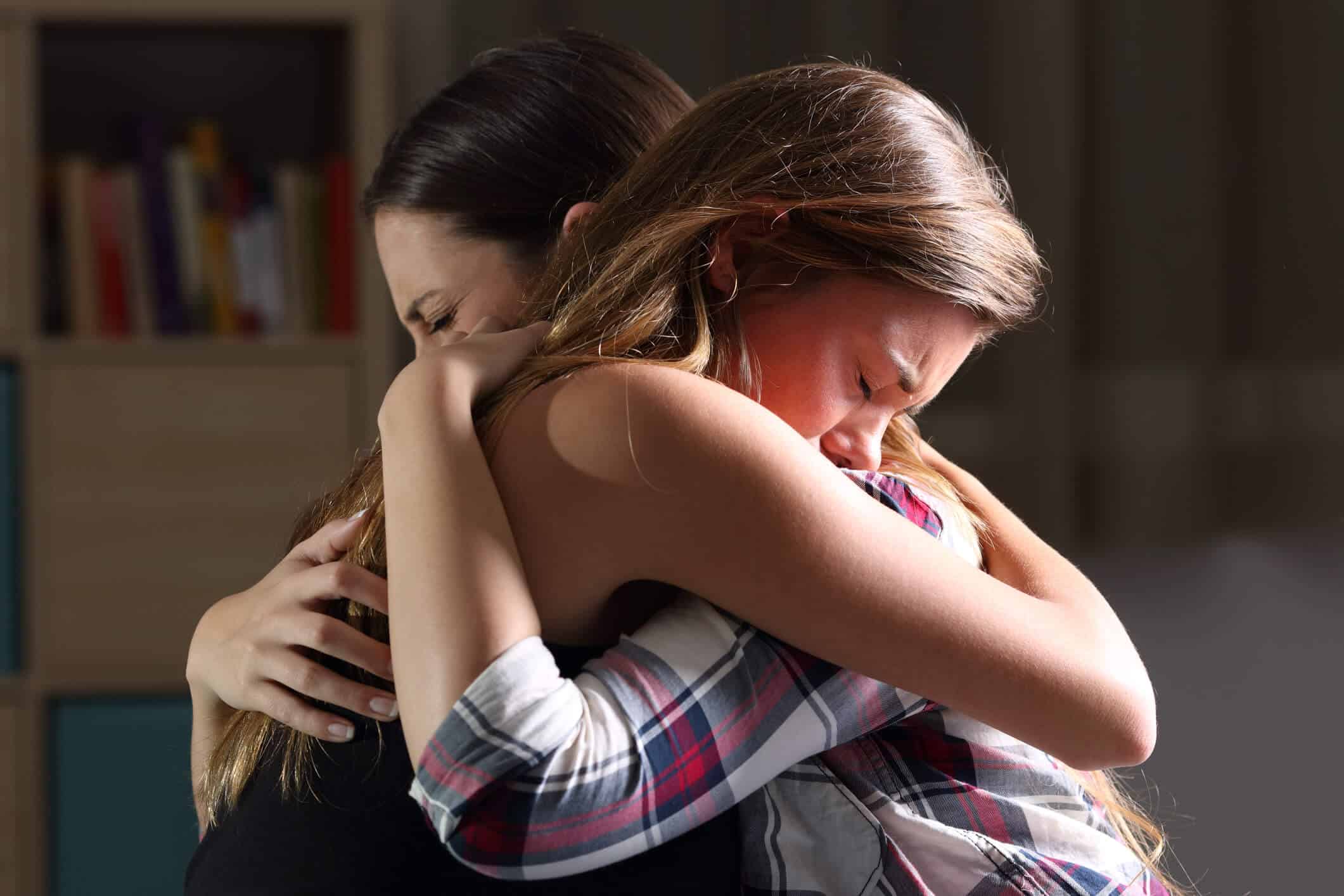Close up profile shot of sad mom hugging her crying teen daughter