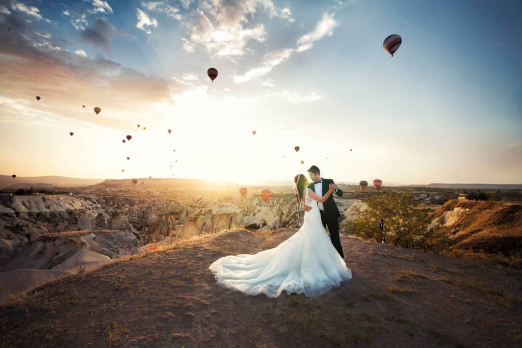 Young newlywed couple dancing at sunrise against the scenic backdrop of a huge canyon and many floating hot air balloons