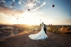 Young newlywed couple dancing at sunrise against the scenic backdrop of a huge canyon and many floating hot air balloons