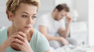 Woman looking pensive with man in background looking sad and frustrated
