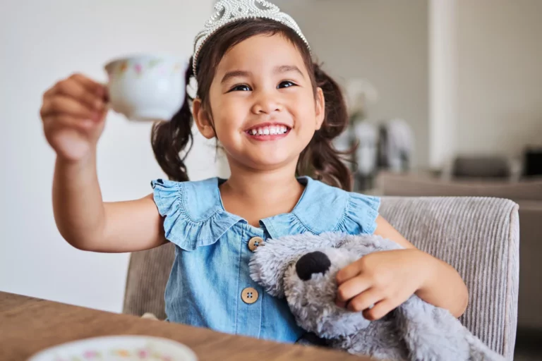 Family traditions: Little girl in a blue dress holding up a tea cup with a big smile