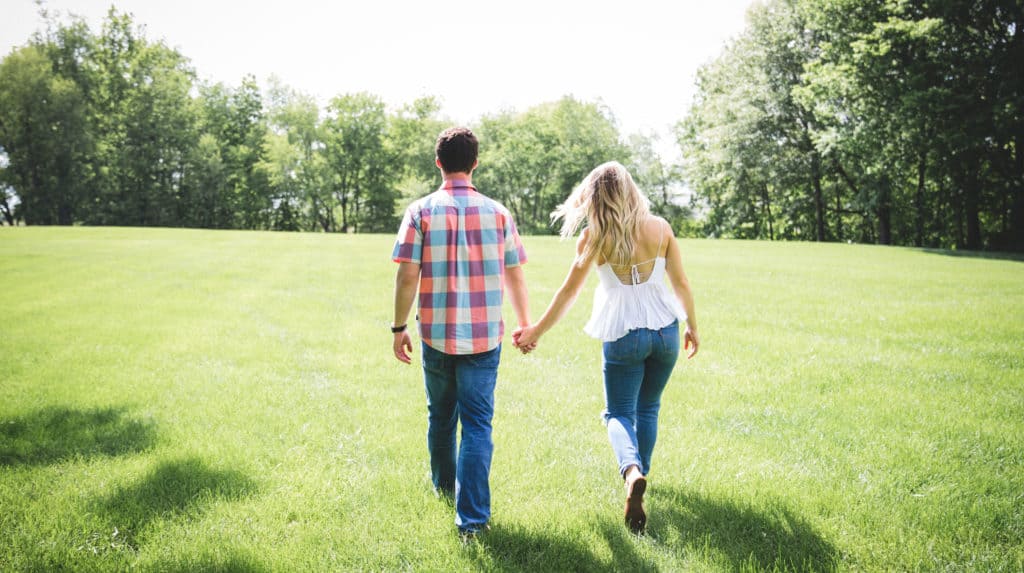 A couple holding hands walks through a park.
