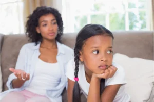 School-age daughter looking away from Mother trying to talk to her while both sit on the couch