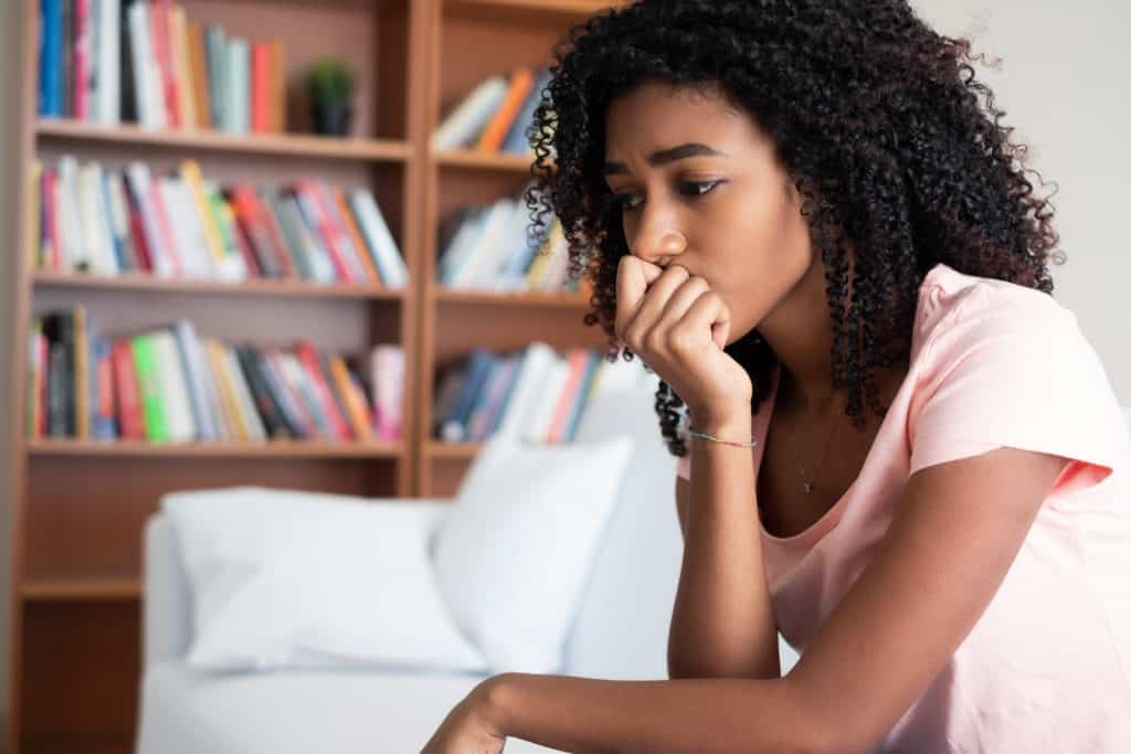 Worried teen girl sitting on a couch staring off camera, contemplating her troubles with her head resting on her hand.