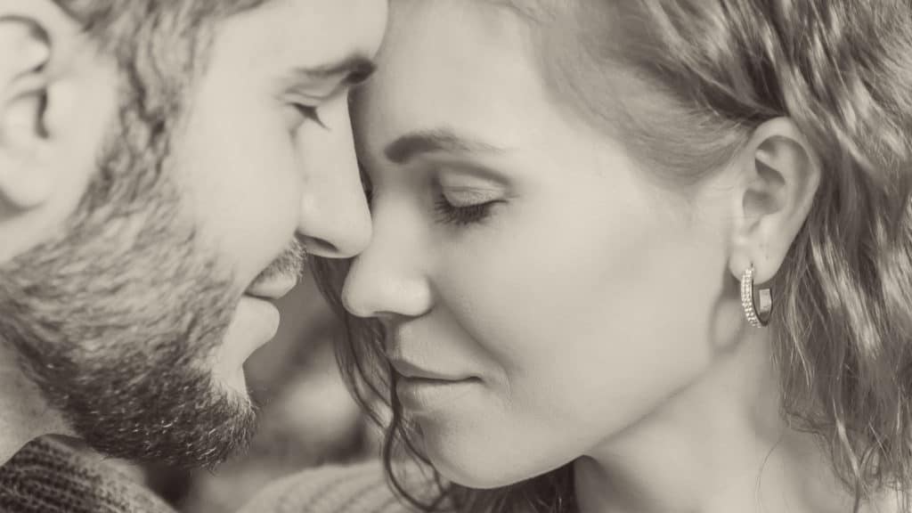 Black and white close up of man and woman face-to-face with their eyes closed and foreheads resting against one other