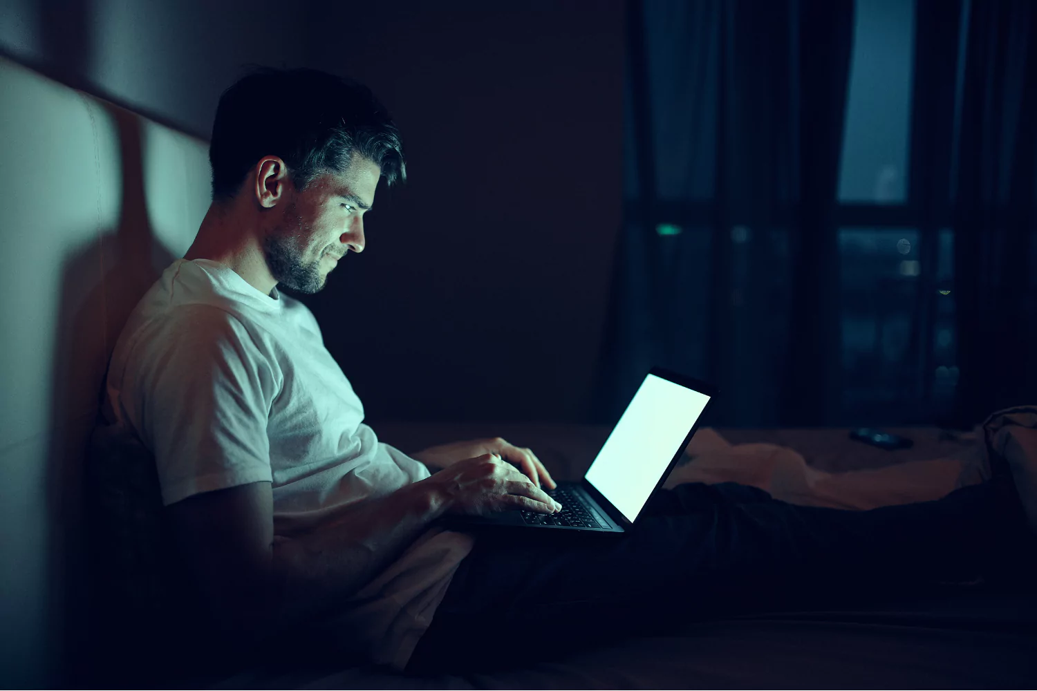 Man looking at computer in dark hotel room